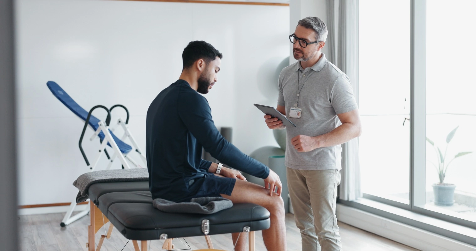 A doctor converses with a seated man in a clinical environment, discussing health matters.